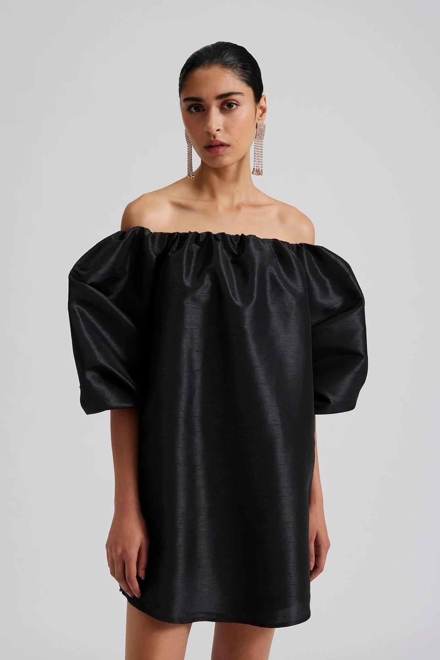 Front facing 2 Malina Off-shoulder black mini dress with short pouf sleeve and wide fit. The perfect addition to your luxury designer resort wear wardrobe.