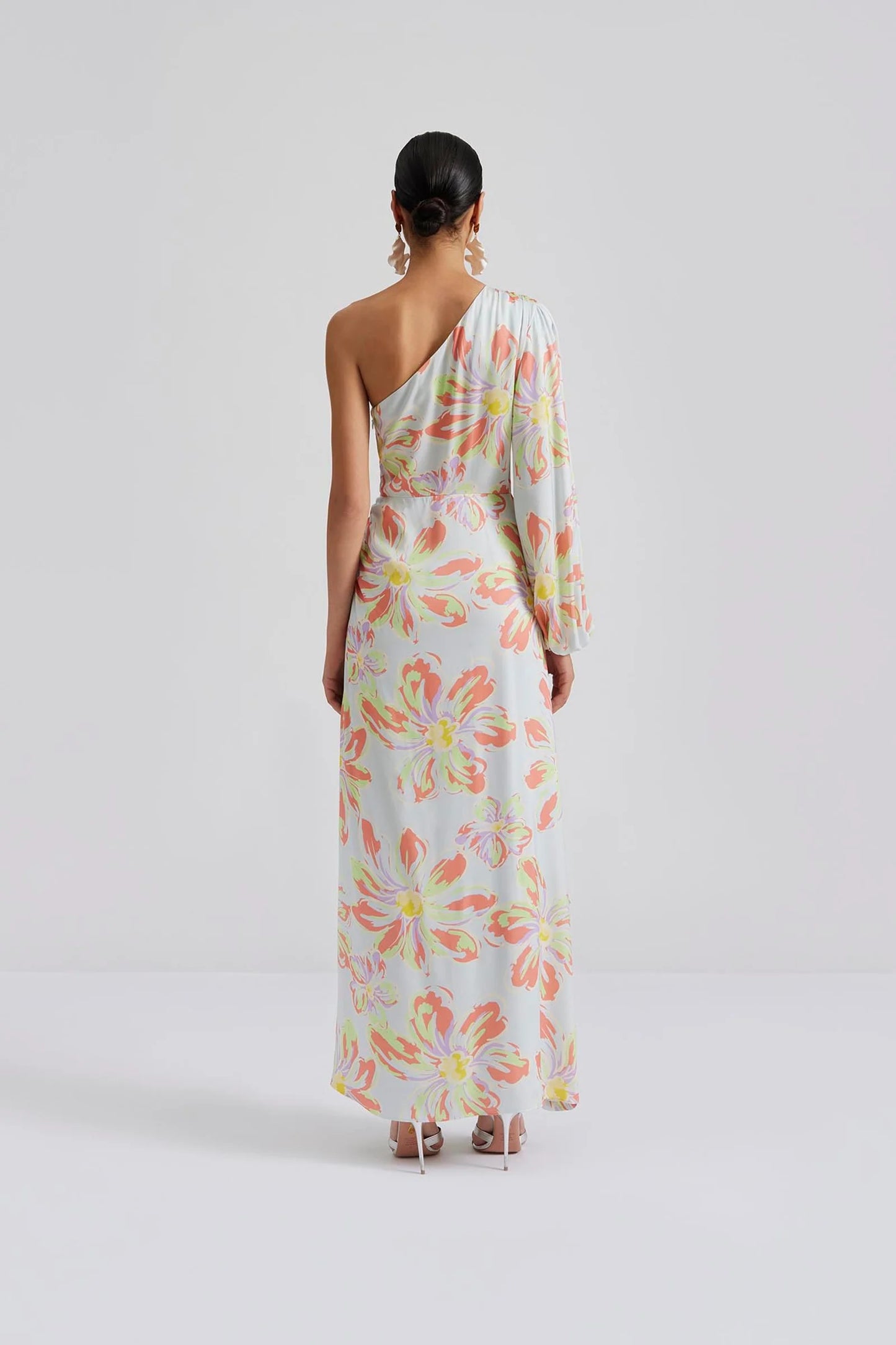 Back facing Malina Printed one shoulder long sleeved maxi dress with ruffle details and slit in the side. Effortlessly elegant and stylish, the Joslin One Shoulder Maxi Dress in Blue Lily is a must-have for any formal occasion. This one-shoulder design features flowy maxi skirt, creating a timeless and sophisticated look. Made with high-quality materials, this dress is both comfortable and chic. The perfection addition to your luxury designer resort wear wardrobe.