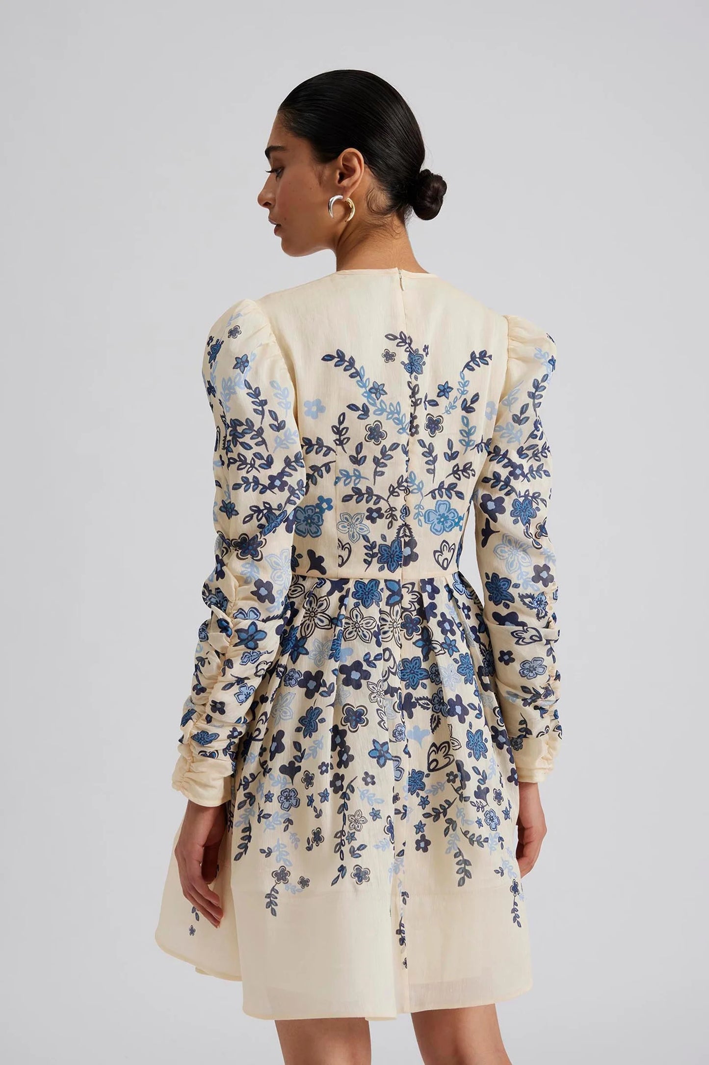 Back facing Malina Printed mini dress with long sleeve in silk blend. Expertly crafted from a luxurious silk blend, this Leoni Mini Dress features a stunning coastal floral design. With its elegant silhouette and soft, breathable fabric, this dress is perfect for any occasion. The perfect addition to your luxury designer resort wear wardrobe.