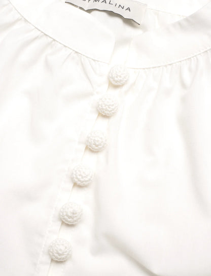 Buttons Malina designer Allie Pouf Sleeve Embroidered Blouse in White. With delicate embroidery and elegant pouf sleeves, this blouse exudes sophistication and exclusivity. Perfect for a luxurious evening out or a high-end event on your next luxury trip to paradise.